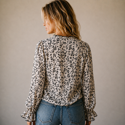 Woman wearing a floral blouse and jeans against a plain background