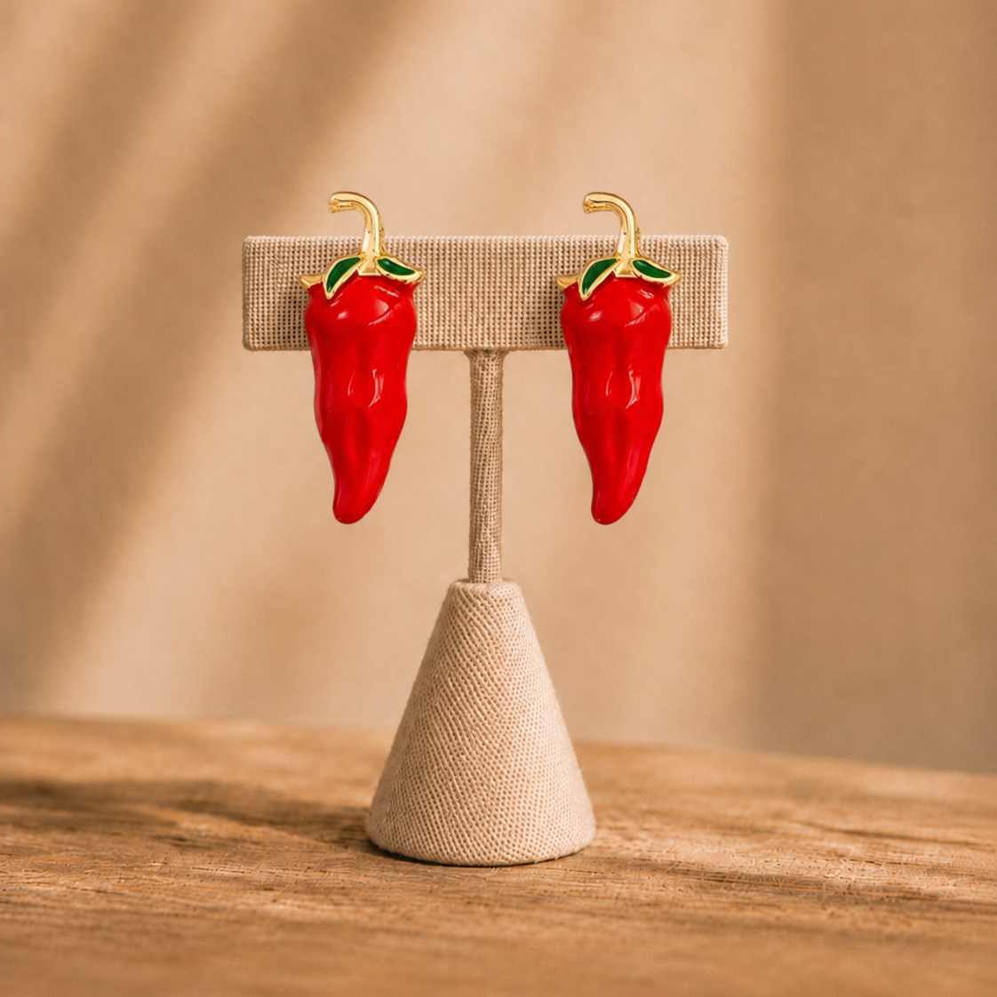 Red chili pepper-shaped earrings on a stand with a beige background