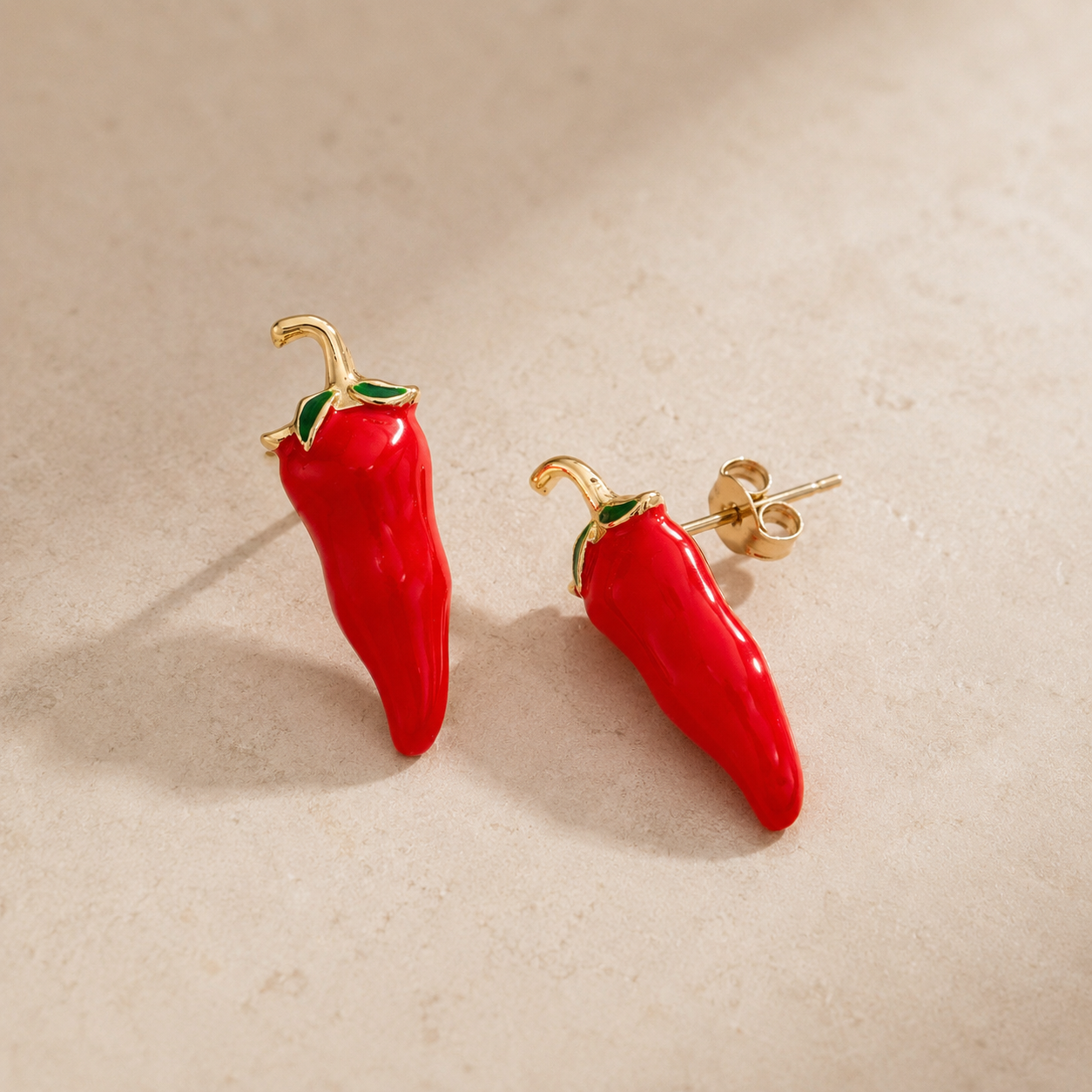 Red chili pepper-shaped earrings on a beige background