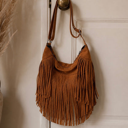 Brown suede handbag with fringe details hanging on a white door.