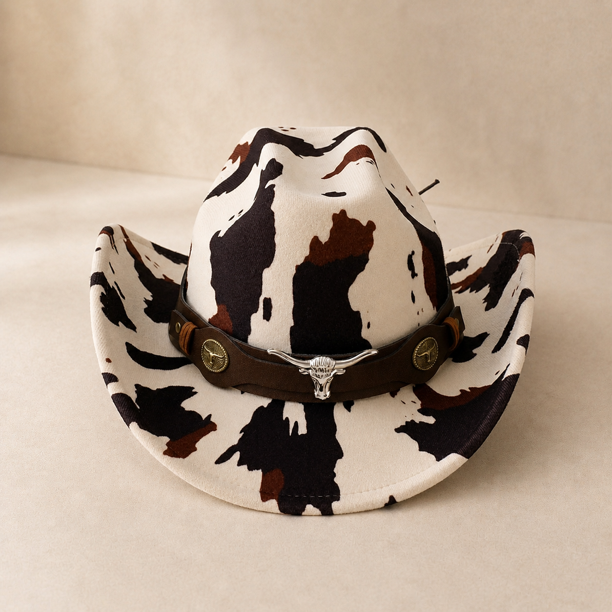 Cow print cowboy hat with a brown band on a beige background